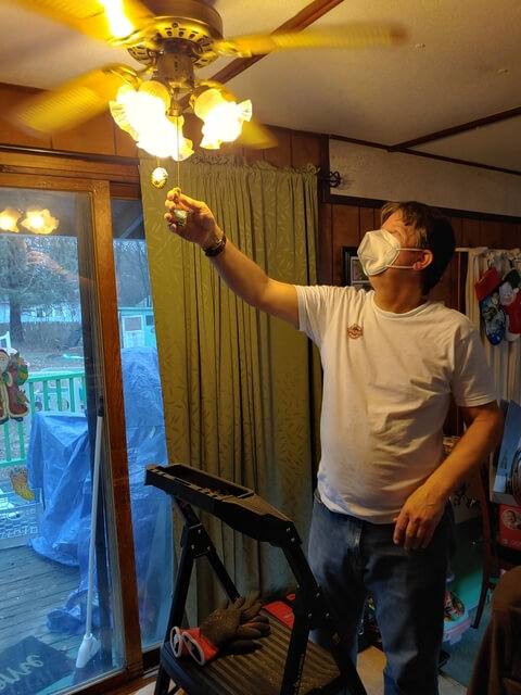 Ed Bartok pulls the chain on a ceiling fan. His stepstool and tools are nearby.