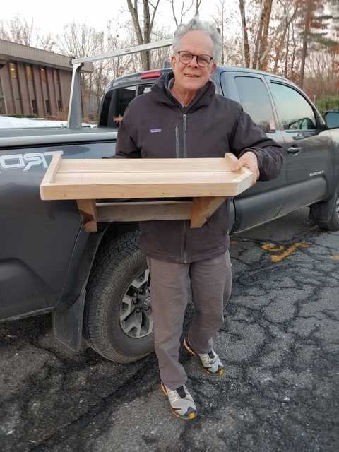 Jed Proujansky holds a wooden shelf while standing by his truck.