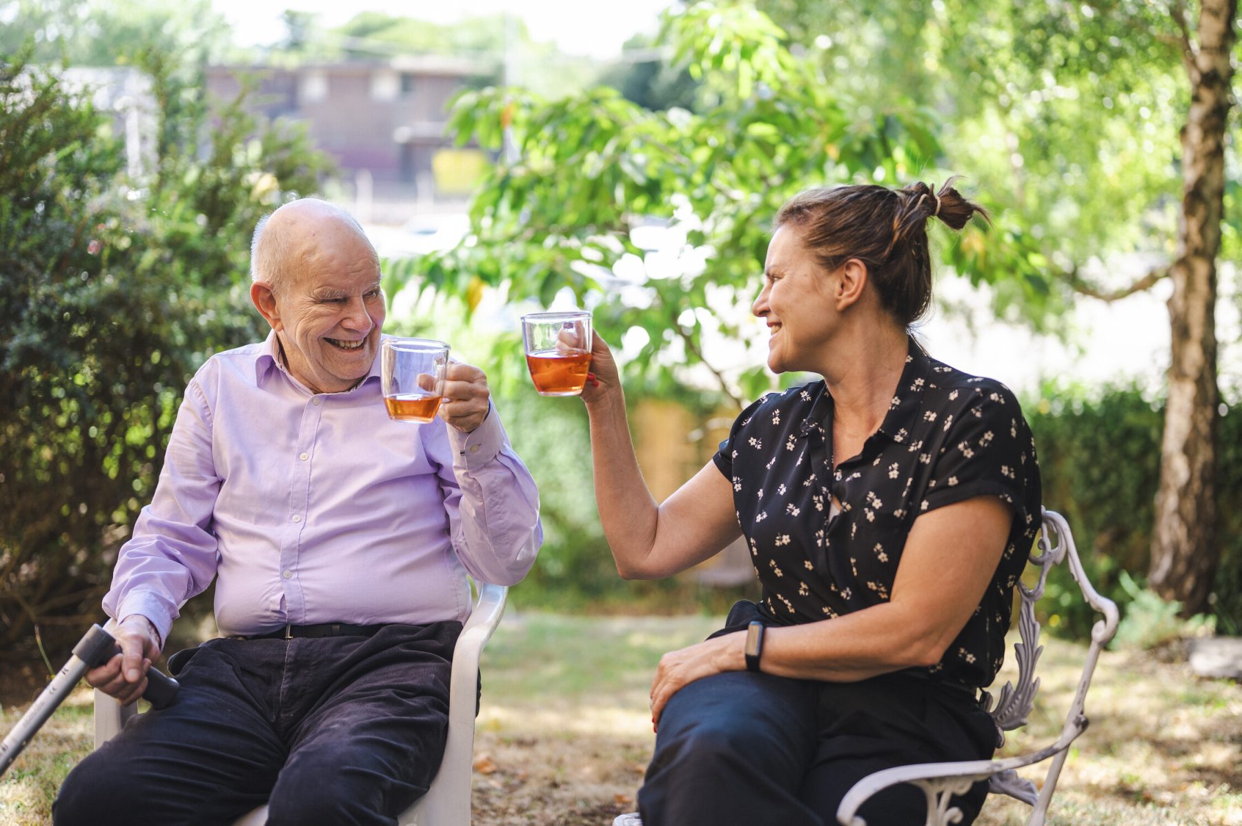 An older man and younger woman toast each other with glasses of tea