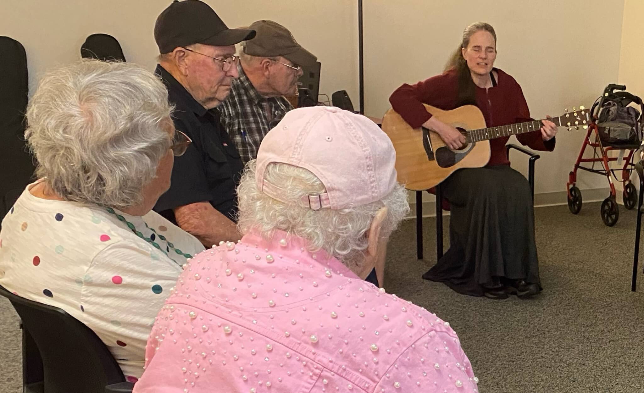 woman playing guitar and singing to seated older adults