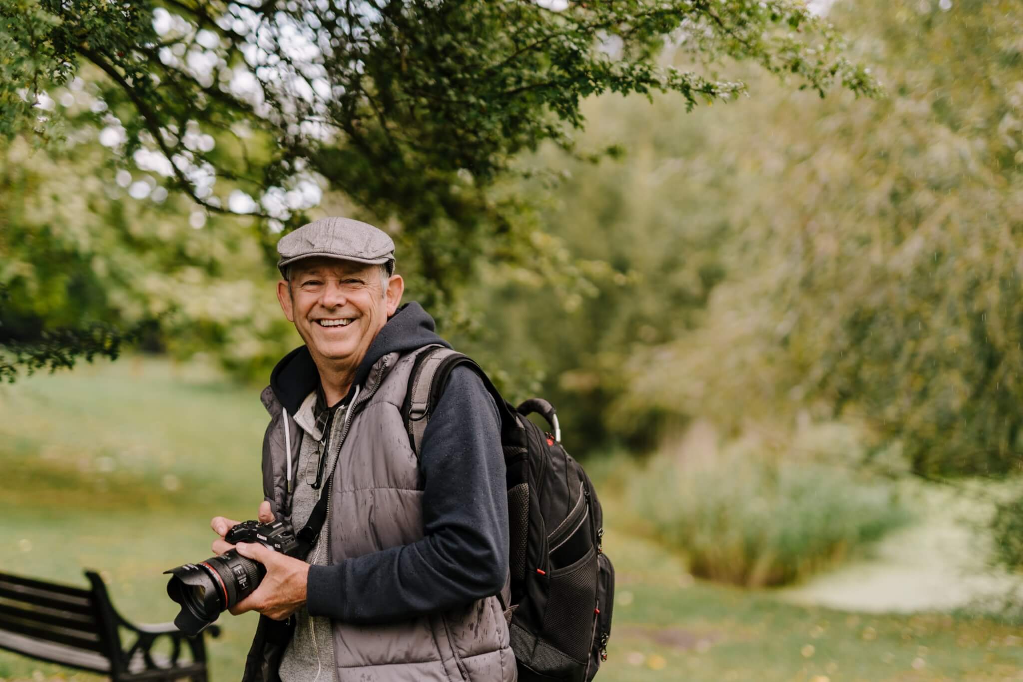 happy older adult standing outside with camera and backpack