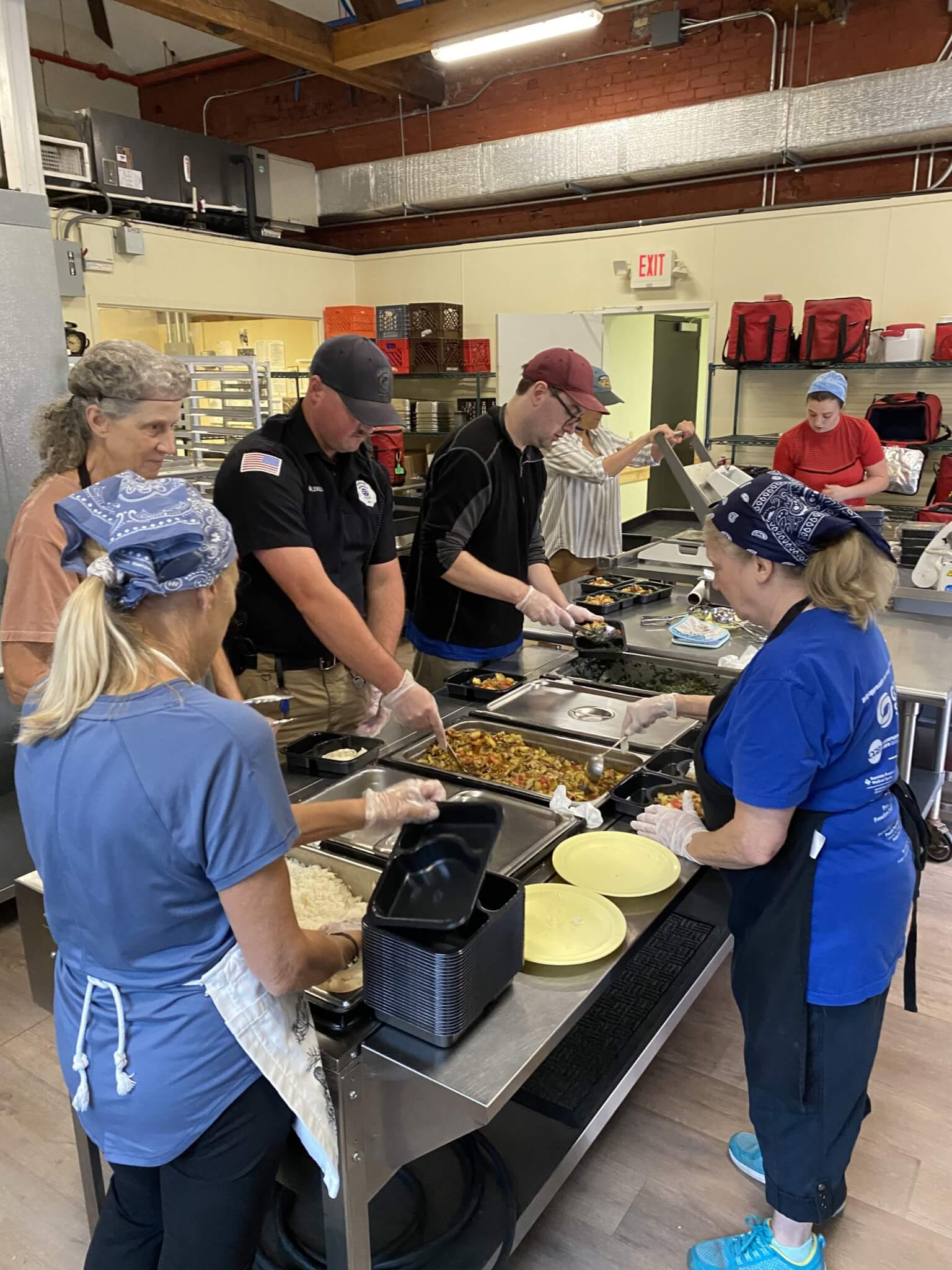 Kitchen staff and a police officer work together to prepare Meals on Wheels