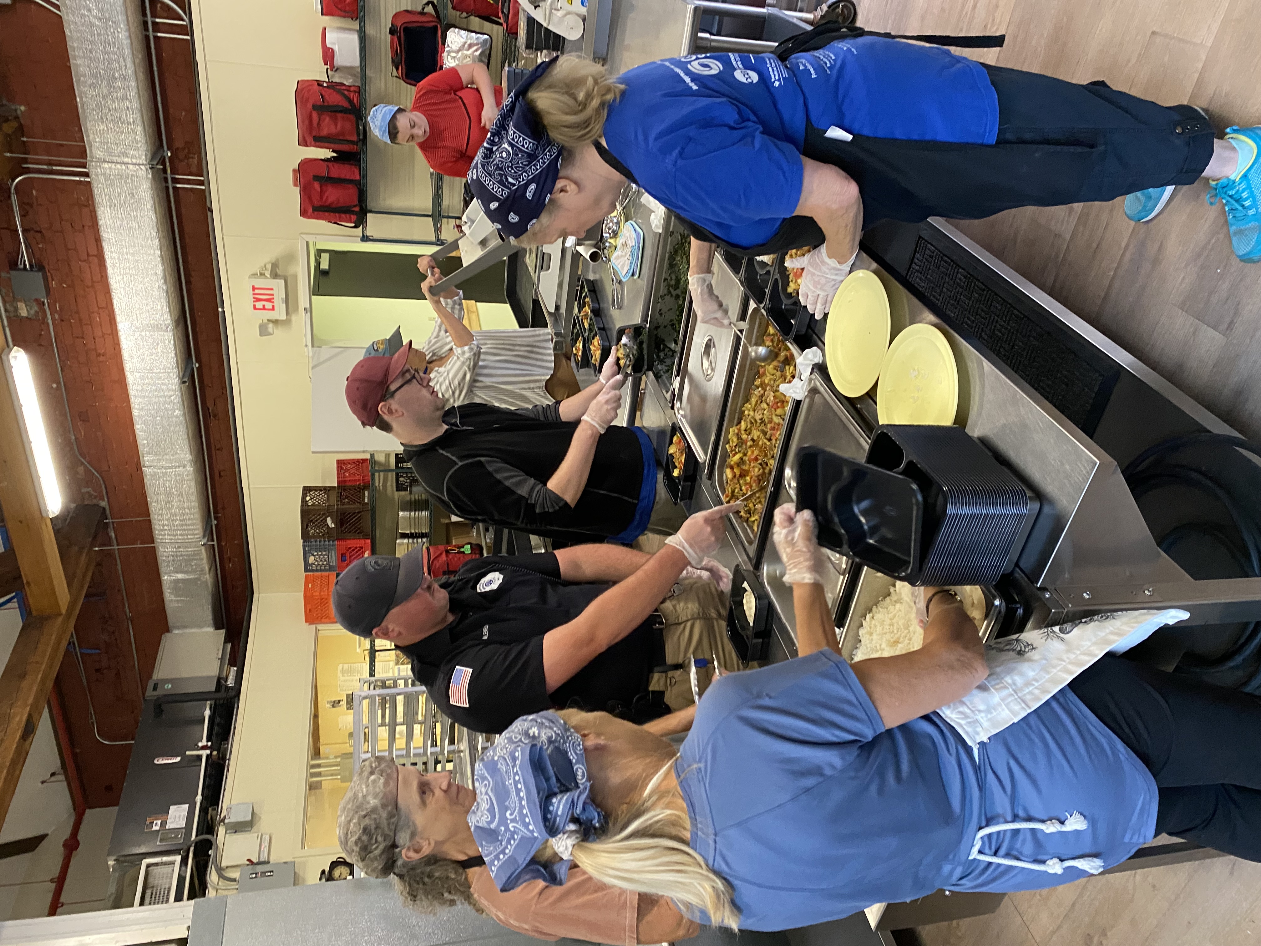 Kitchen staff and a police officer work together to prepare Meals on Wheels