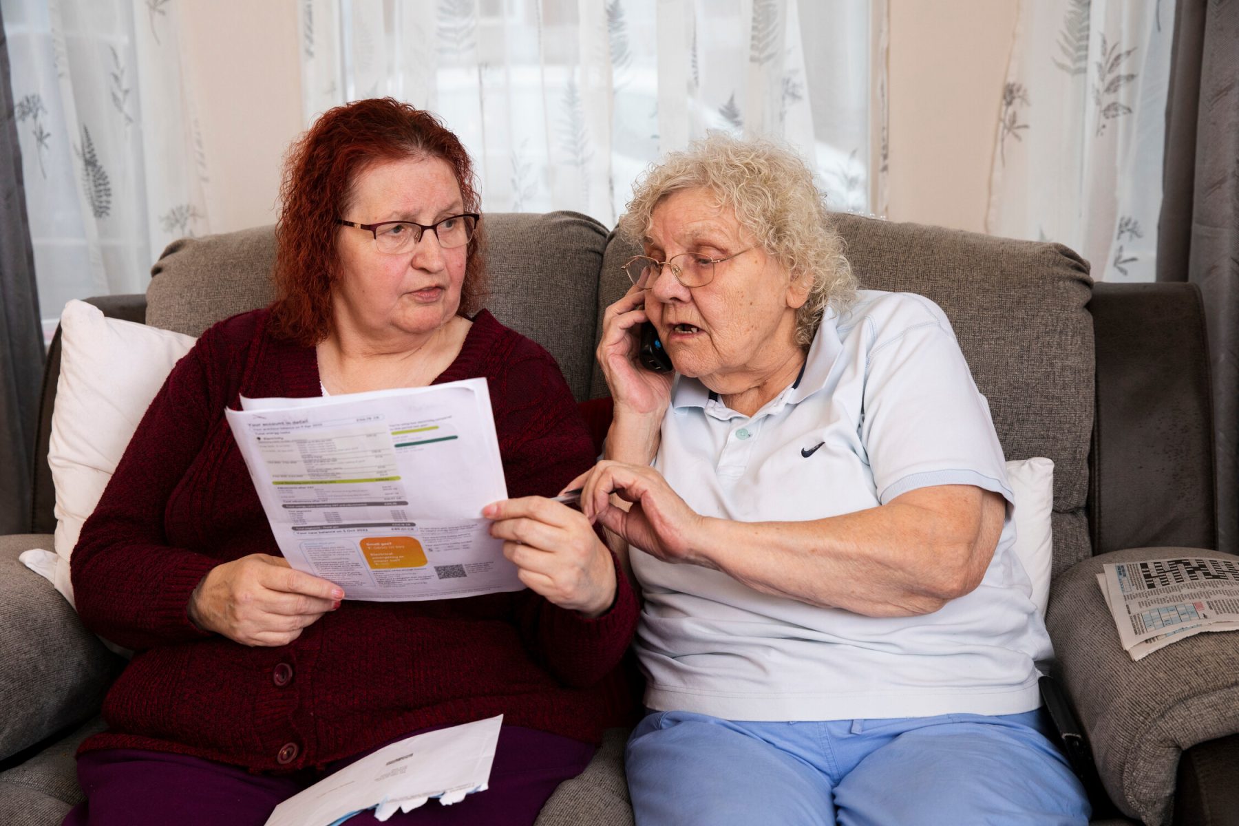 An older couple of two women reviews bills and makes a phone call.