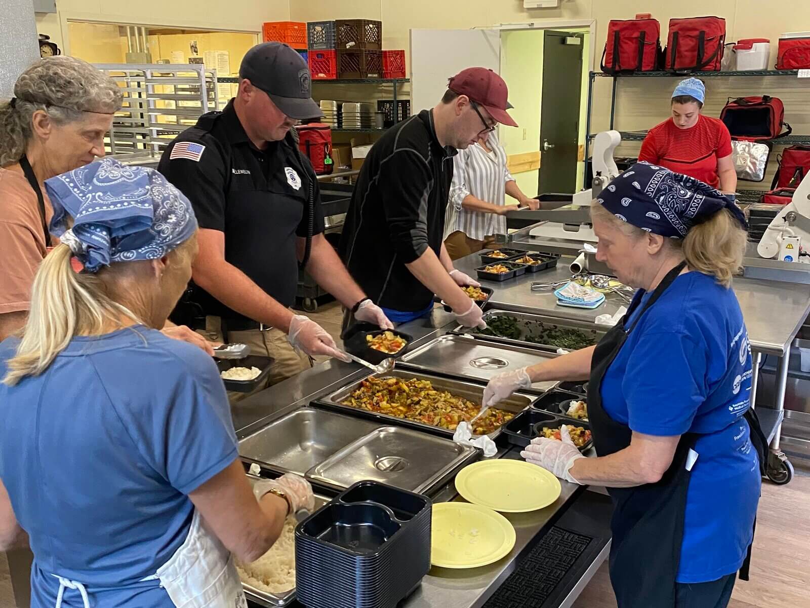 Officer Llewelyn helping prepare meals in the Meals on Wheels kitchen with staff.