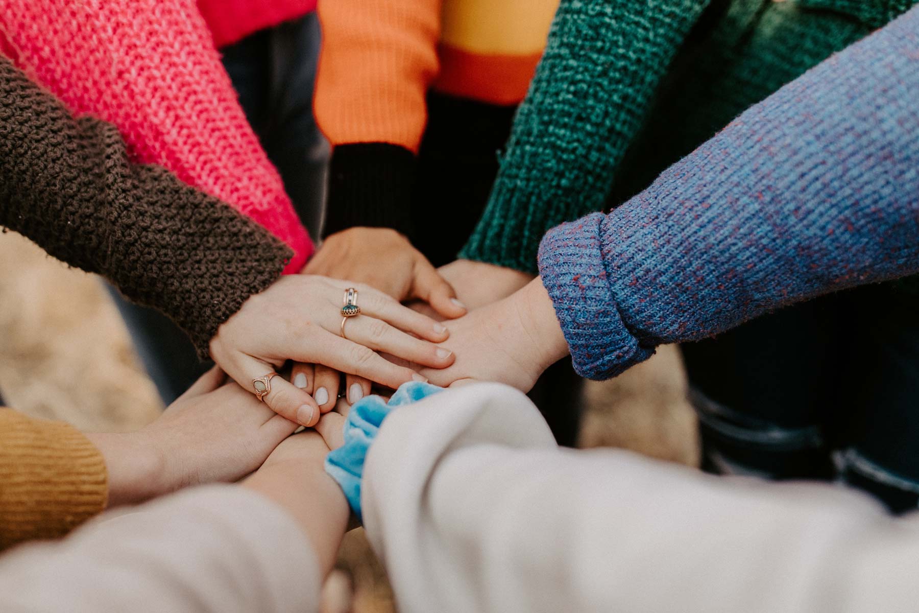 A team of people piles their hands together, wearing differently colored sweaters