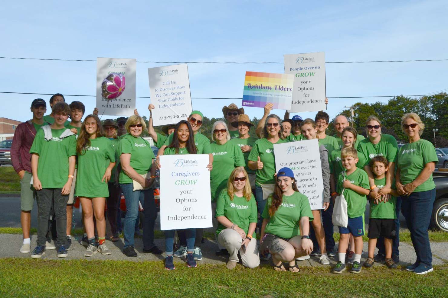 Large group of LifePath people in green t-shirts holding rainbow signs