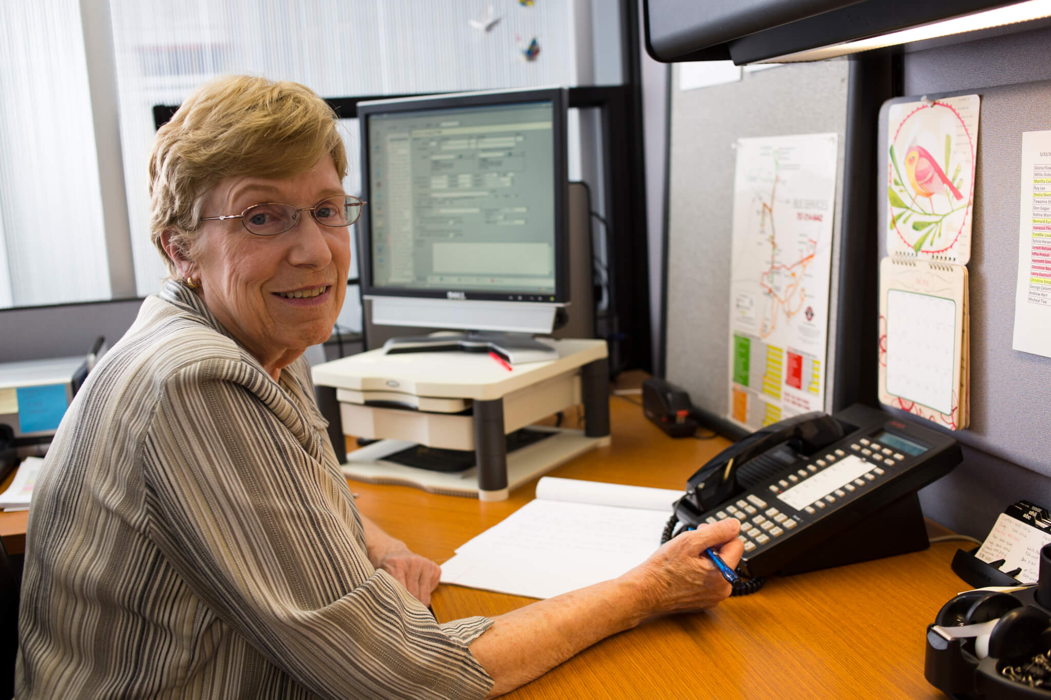 older woman smiling at her desk by a phone