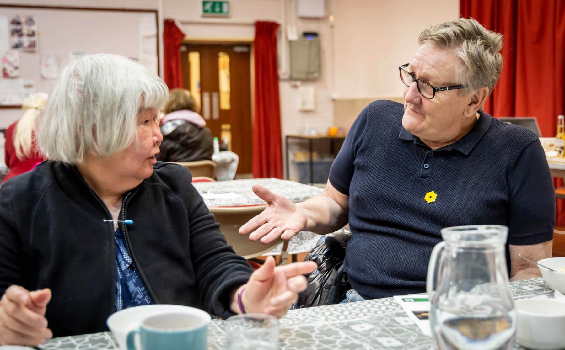 Two older adults having a conversation at a dining table