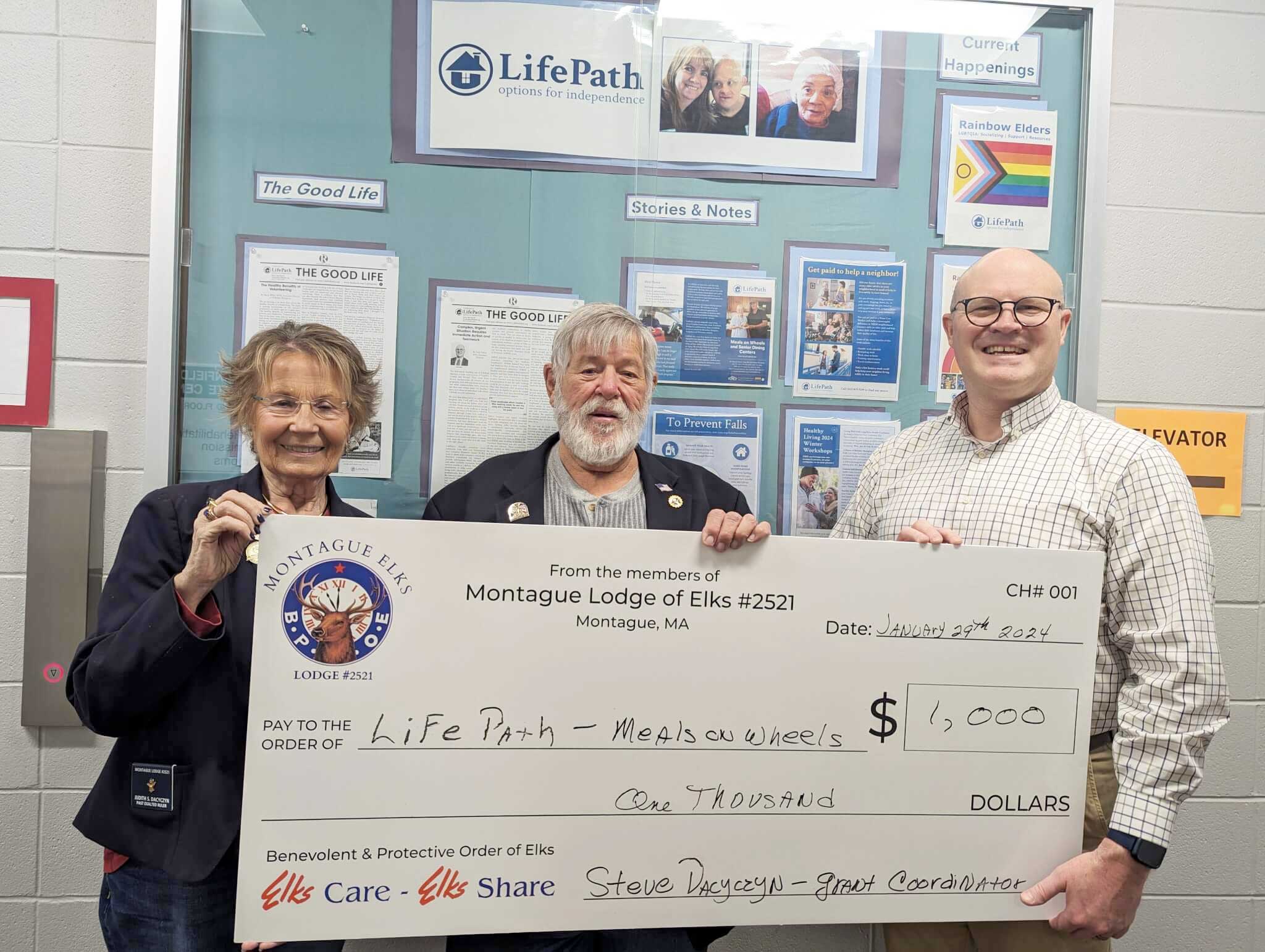 Judy and Steve Dacyczyn presenting a large size check on whiteboard to Executive Director Gary Yuhas.