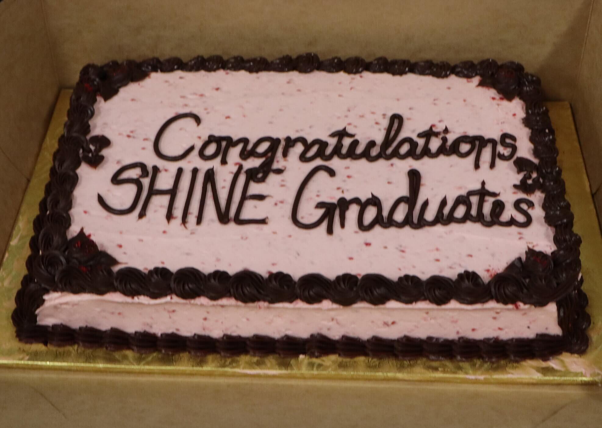 cake with pink frosting and brown lettering saying "Congratulations SHINE Graduates"