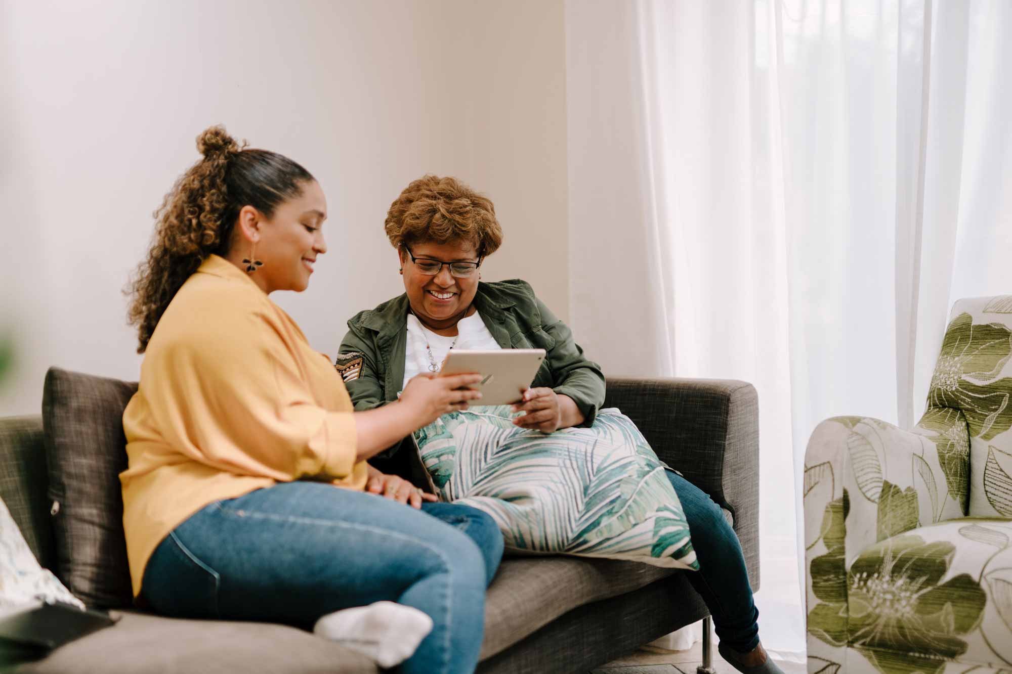 An older and younger woman use a tablet on the couch together