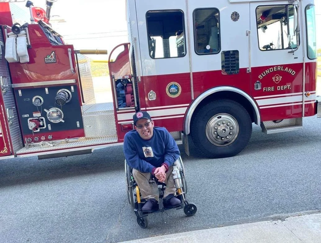 Man in wheelchair in front of firetruck smiling