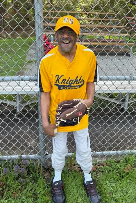 A man in a yellow baseball uniform smiling and holding a baseball glove.