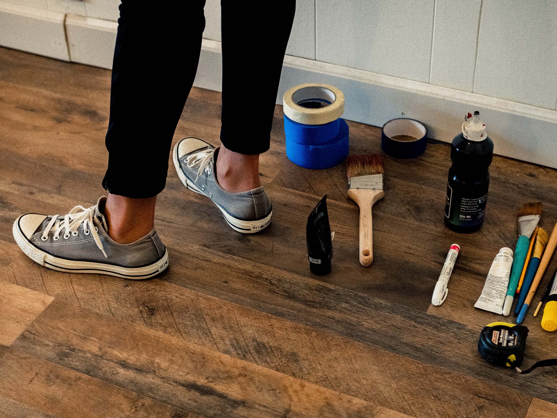 Painting and repair tools near a person's feet on a wooden floor
