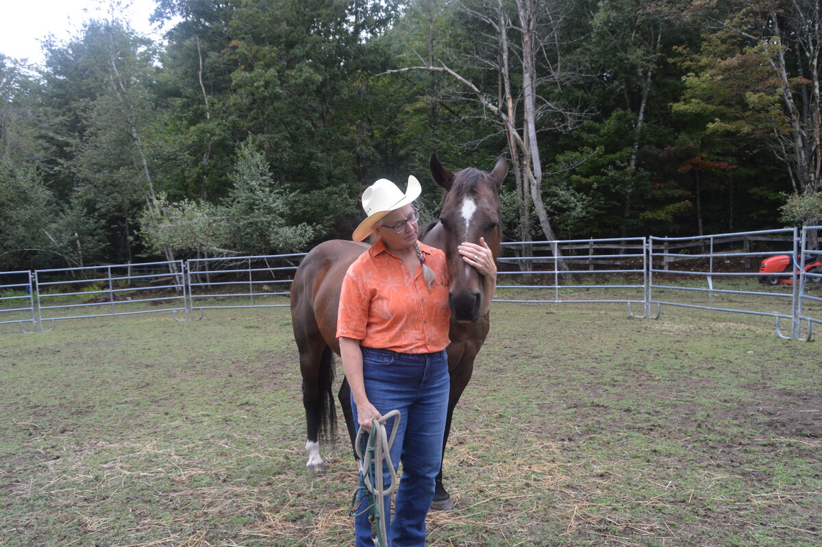 Elizabeth stands in a paddock with Sadie the horse, stroking her nose