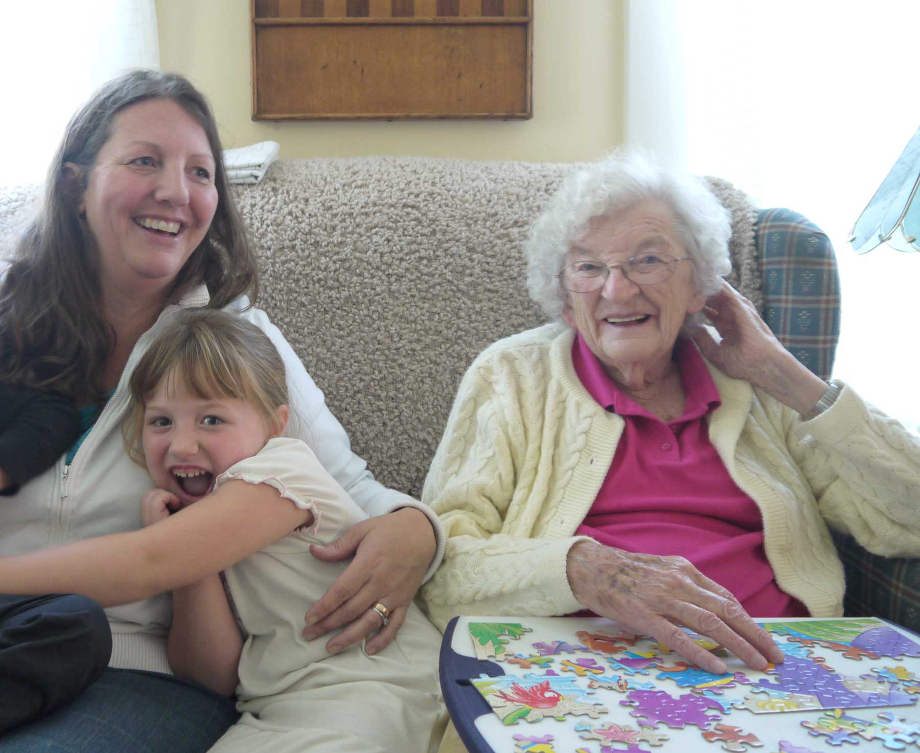 A woman with young children sits on a couch with an older woman, working on a puzzle