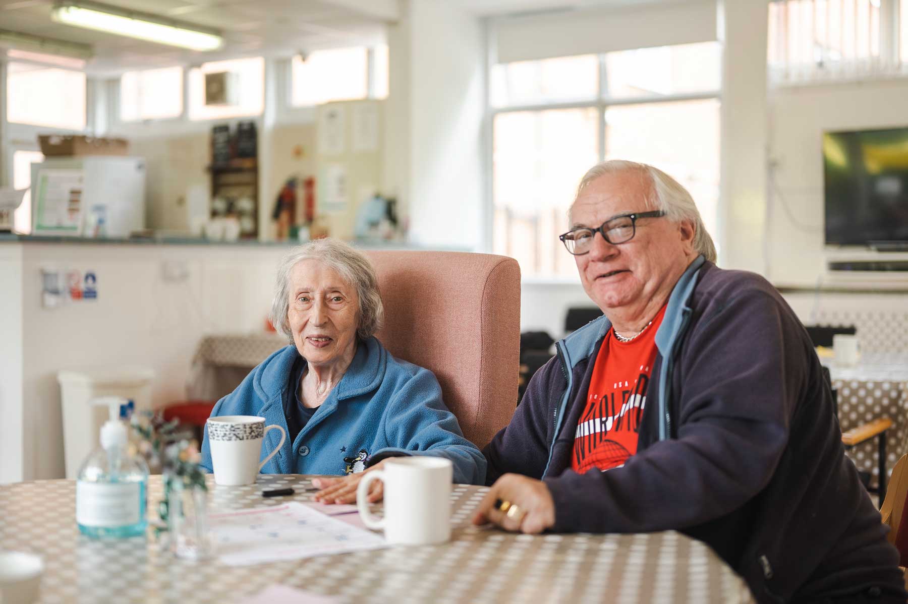 Two older adults sit at a dining table together